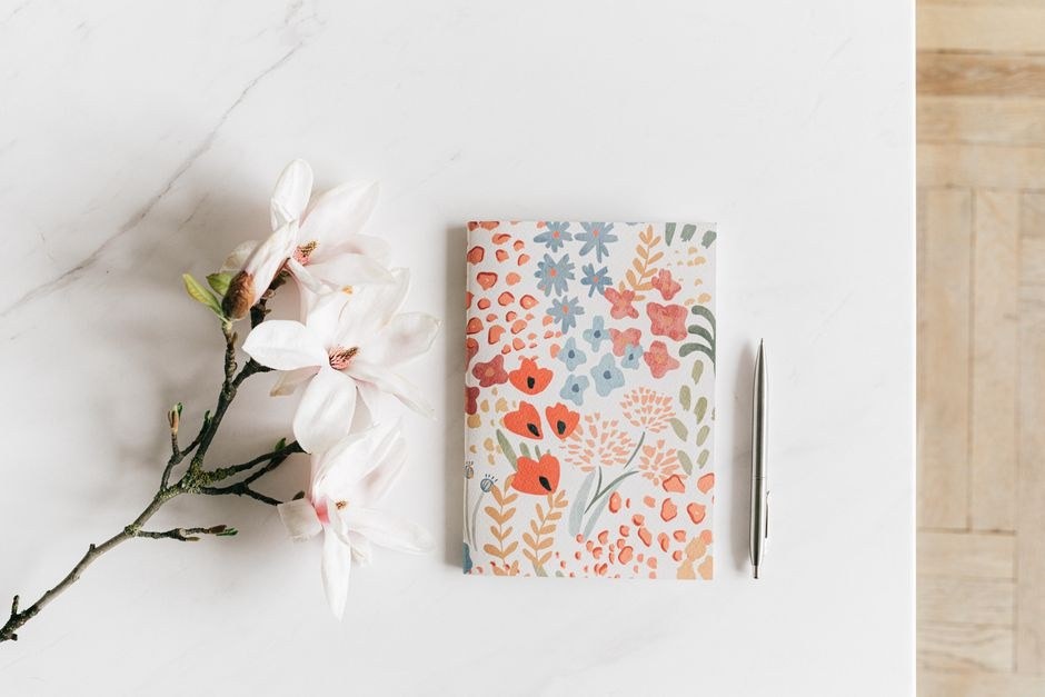 A patterned notebook and pen arranged on a light desk